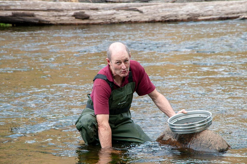 Man dressed in waders fossicking for gemstones in a Tasmanian river