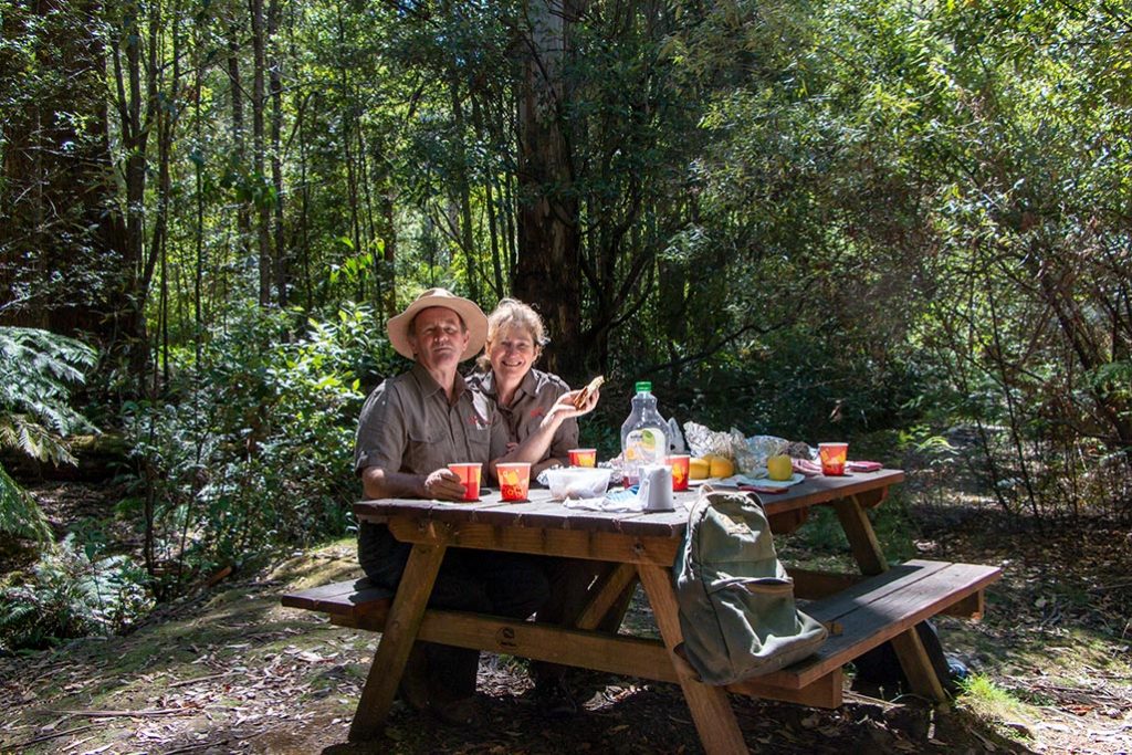 Man and woman sitting at a picnic table in a bush setting
