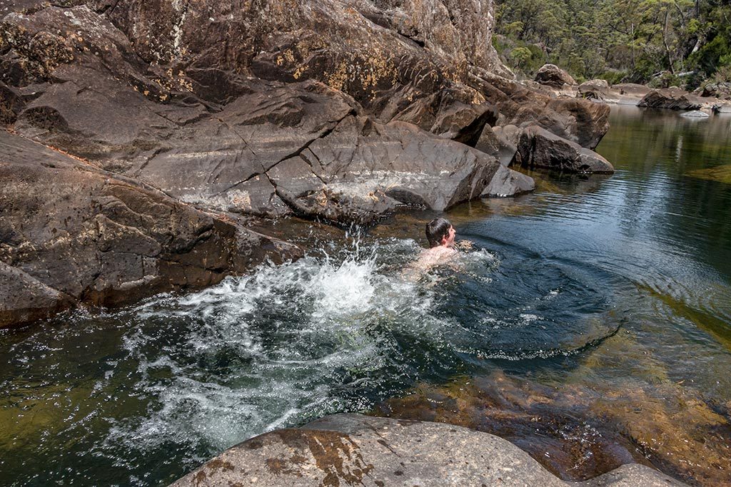 Young boy swimming in a deep rock pool making big kicking splash