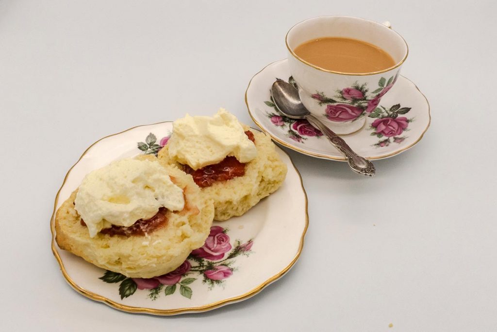 A cup of tea with a plates of scones jam and cream