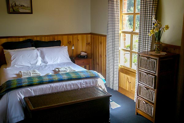 Queen bed with slight streaming in the window in Fon Hock cottage accommodation near Derby in Tasmania