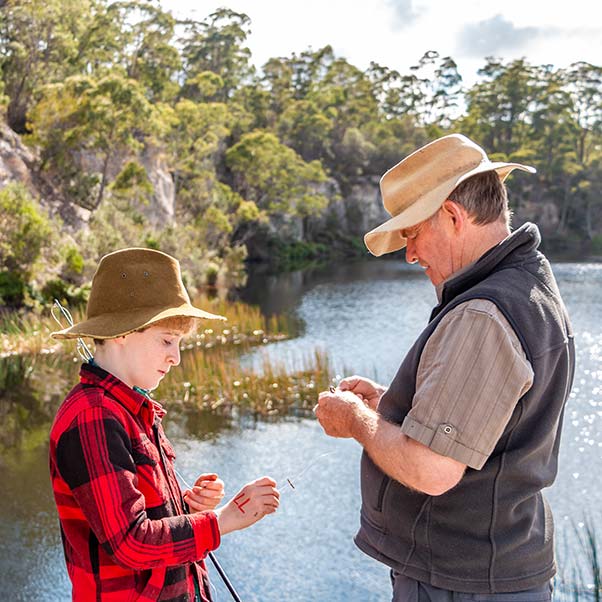 A young boy and his farther placing bait on a fishing line with a fresh-water lake in the background.