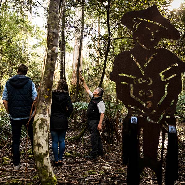 A steel silhouette is in the foreground and in the background are three people looking up at the trees.