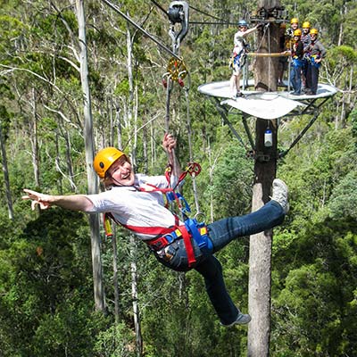 A woman flying between two tree-top platforms on a zip-line.