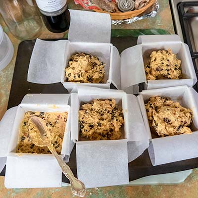Five small cake tins lined with baking paper sitting on the kitchen bench. Each cake has some cake mix added.