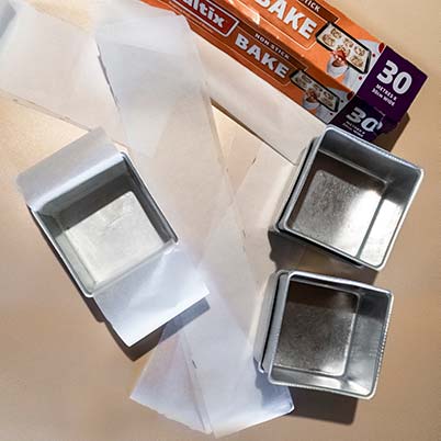 Strips of baking paper and three baking tins on a table.