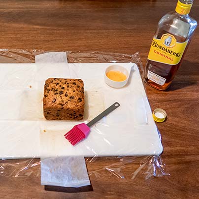 One cake is sitting on a white board next to a basting brush and a bottle of rum.