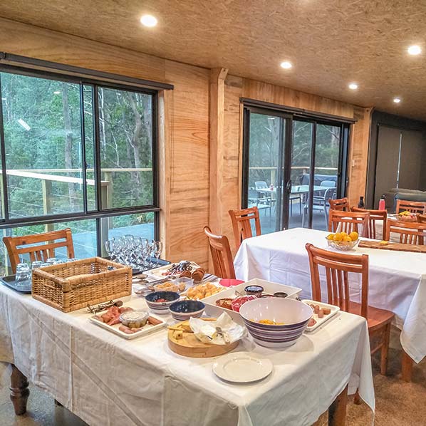 Inside the Barn showing a table set with food and the view out the large window to the wide deck and native bush.
