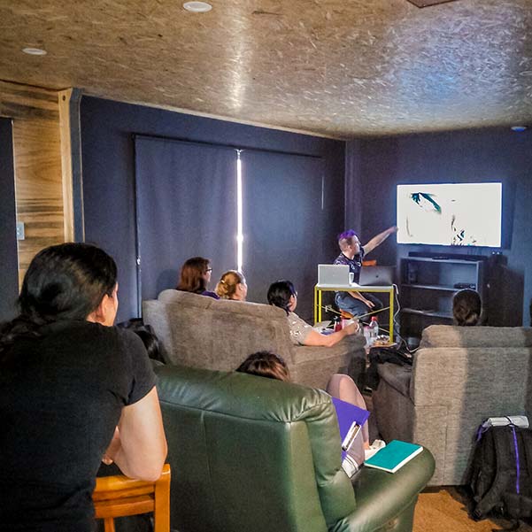 Inside the Barn, Craig is presenting images on the wall screen while participants, sitting in lounge chairs are watching.