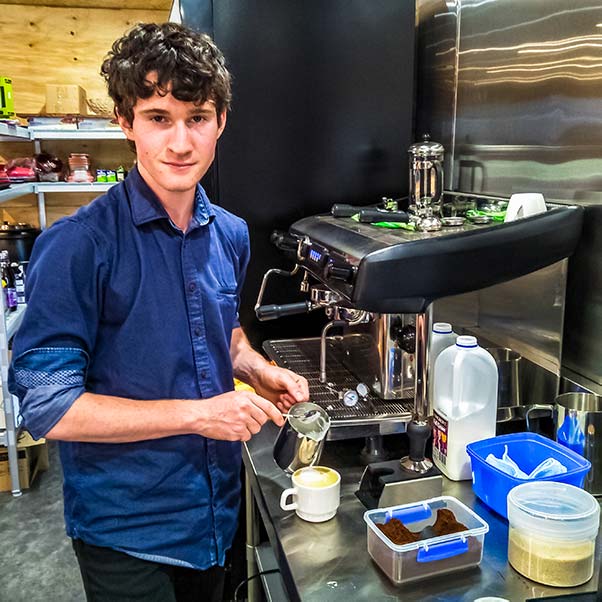 A young man is pouring a cappuccino inside the Barn.