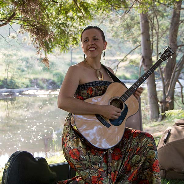 Liz Frencham playing guitar on the bank of the Ringarooma River at Tin Dragon Cottages.