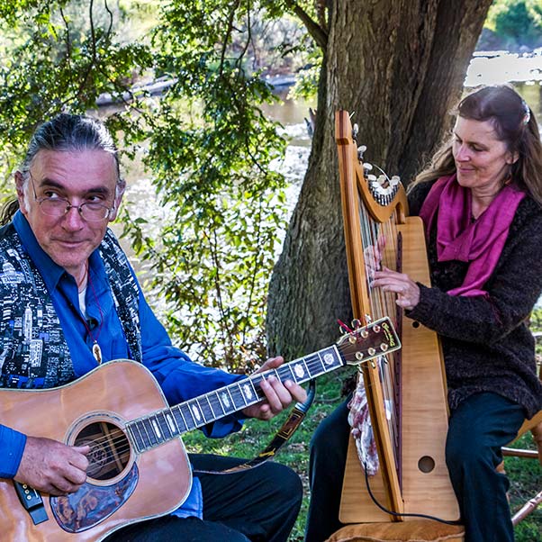 Frank playing guitar and Kate playing harp on the banks of the Ringarooma River at Tin Dragon Cottages.