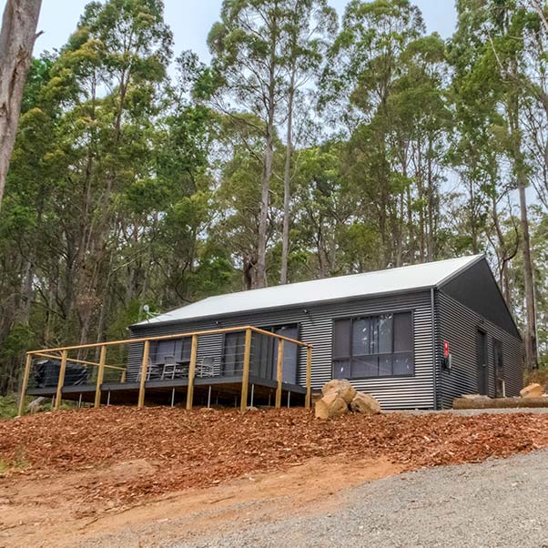 This charcoal coloured tin barn set in native bush has a large front deck. It is ideal for family holidays.