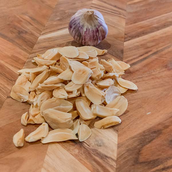 A pile of dehydrated garlic bulbs are sitting on a wooden cutting board. This is one method to store garlic.
