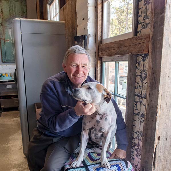 Graham sitting on a bench inside the Swinging Gate Vineyard Cellar is cuddling a dog.