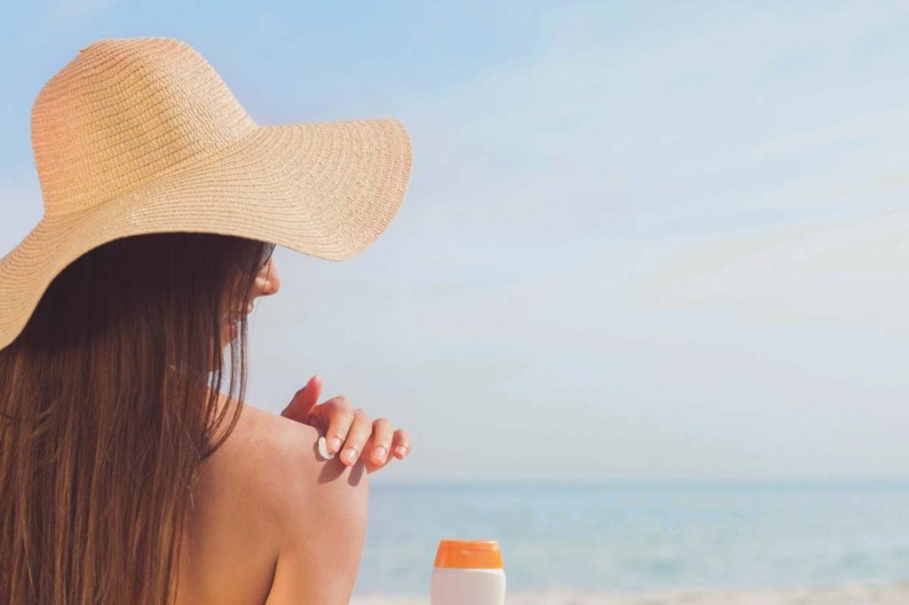 Woman at a beach with a large straw hat facing the ocean.
