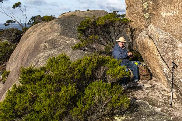 Graham is sitting beneath the cube rock in a sheltered area.