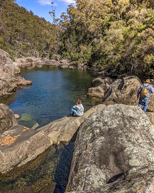 Swantje sitting on a large rock looking down into a very clear rock pool on the St Pauls River above Meadstone Falls.