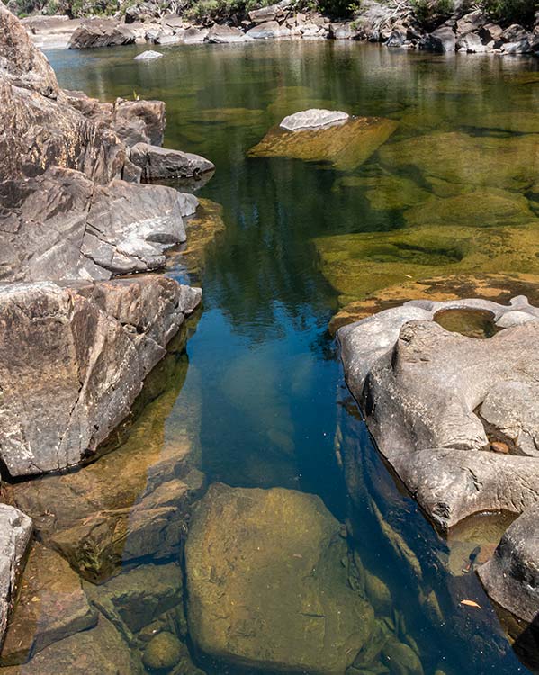 Looking down into the deep clear water of the rock pool. The water has a bluish-green tinge  but is  crystal clear. The rocks beneath the water a clearly visible.