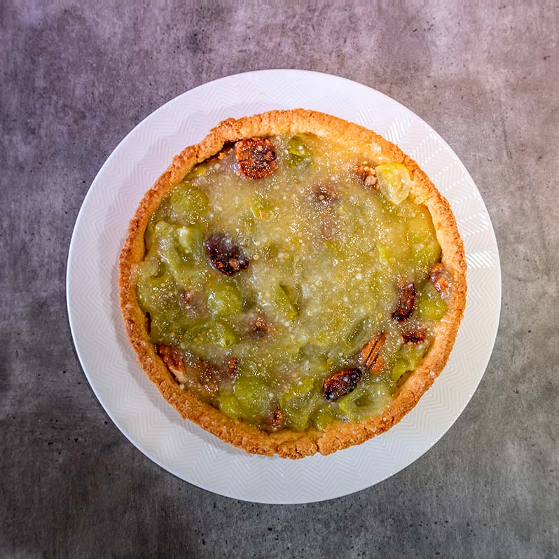 Tomatillo tart sitting on a white plate with a grey background.