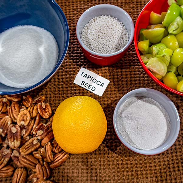 A display of all the ingredients used in cooking the tart; sugar, tapioca, cut tomatillos, pecan nuts and an orange.