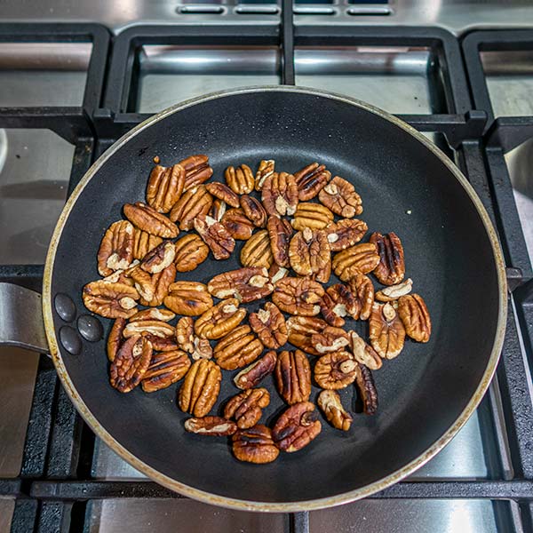 Pecan nuts are being dry-fried in a pan on a gas stove.