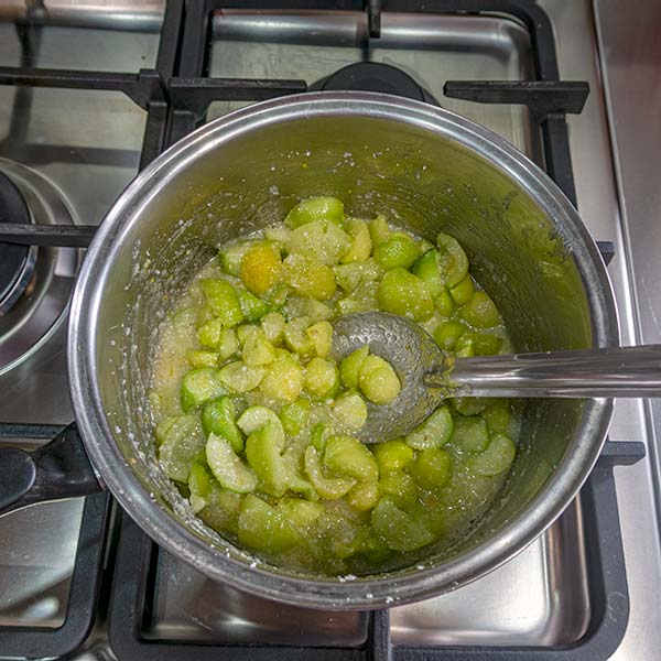 The saucepan of cut fruit, sugar and zest is being stirred over a gentle heat.