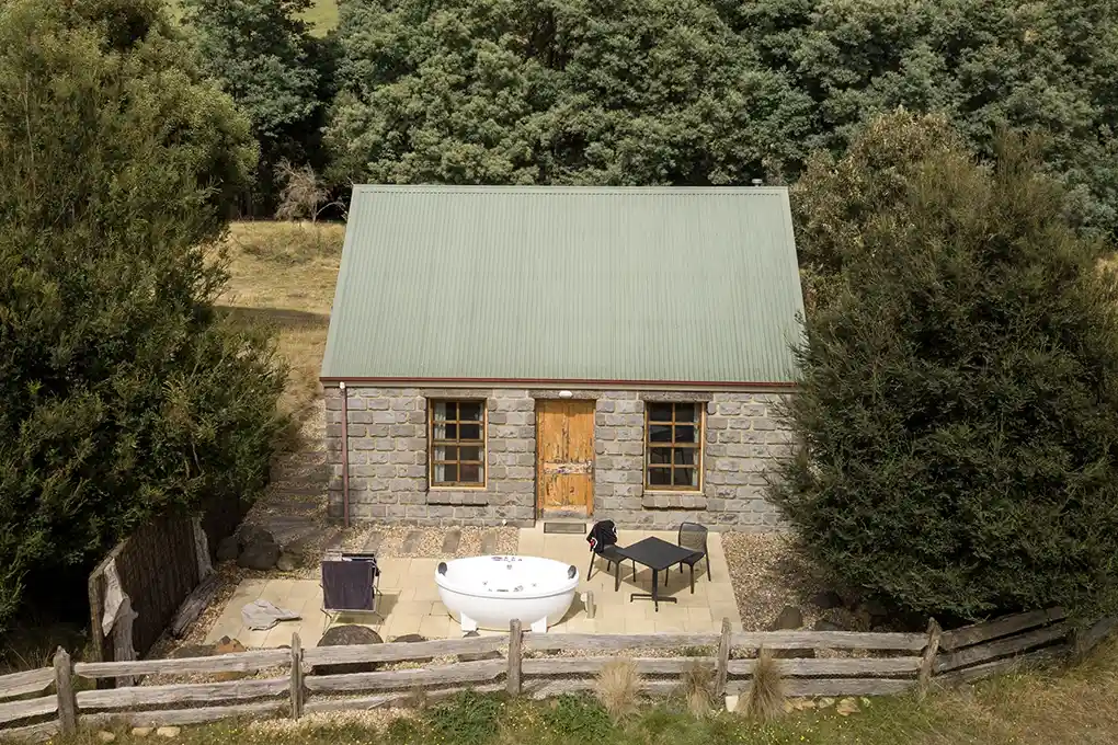 This is an external view of Ah Back studio cottage showing the paved BBQ area with outdoor spa and shrubs.