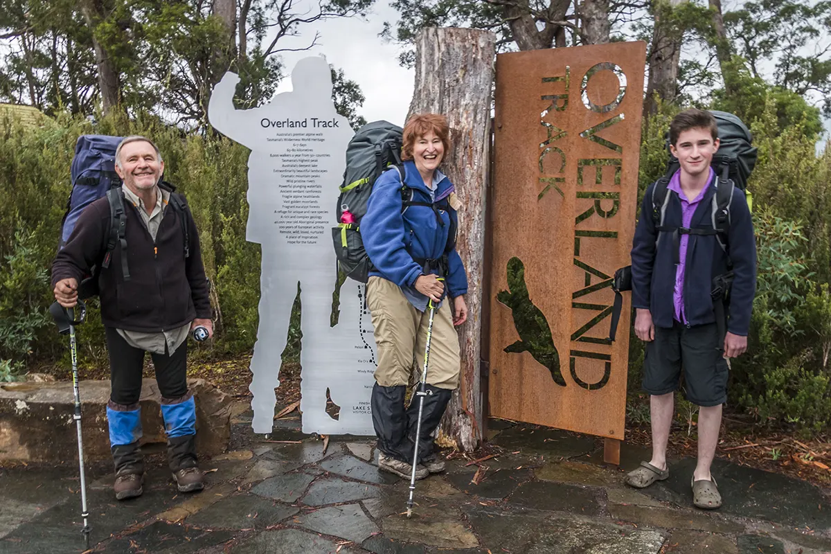 Graham, Christine and James standing in front of the iconic Overland Track sign at Lake St Clair.