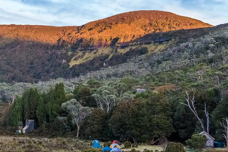 Waterfall valley just after sunrise. There are tents in the foreground.