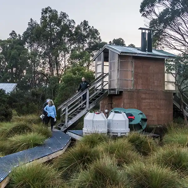 Three people are waiting outside the above ground pod-style toilet at Kia Ora.