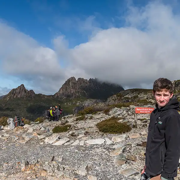 James at Marion's Lookout is standing in front of a "keep off the grass" sign. There are tourists taking selfies in the background standing on the sensitive rehabilitation area.