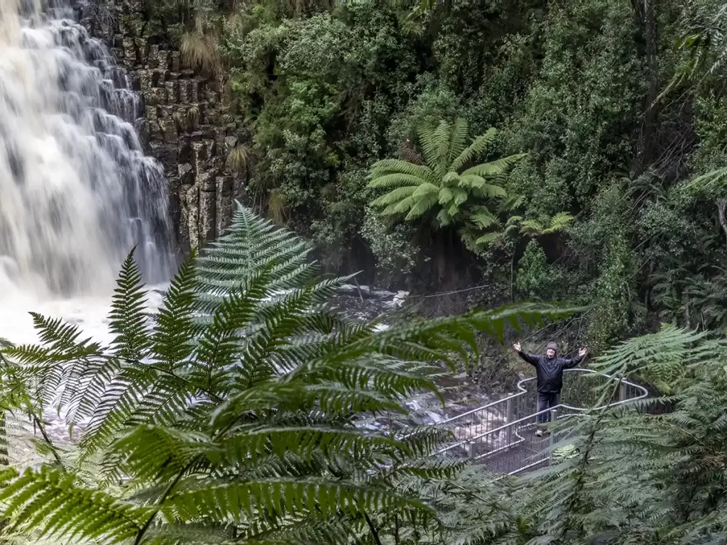 Graham is standing on a platform at the base of a gushing waterfall in North West Tasmania.