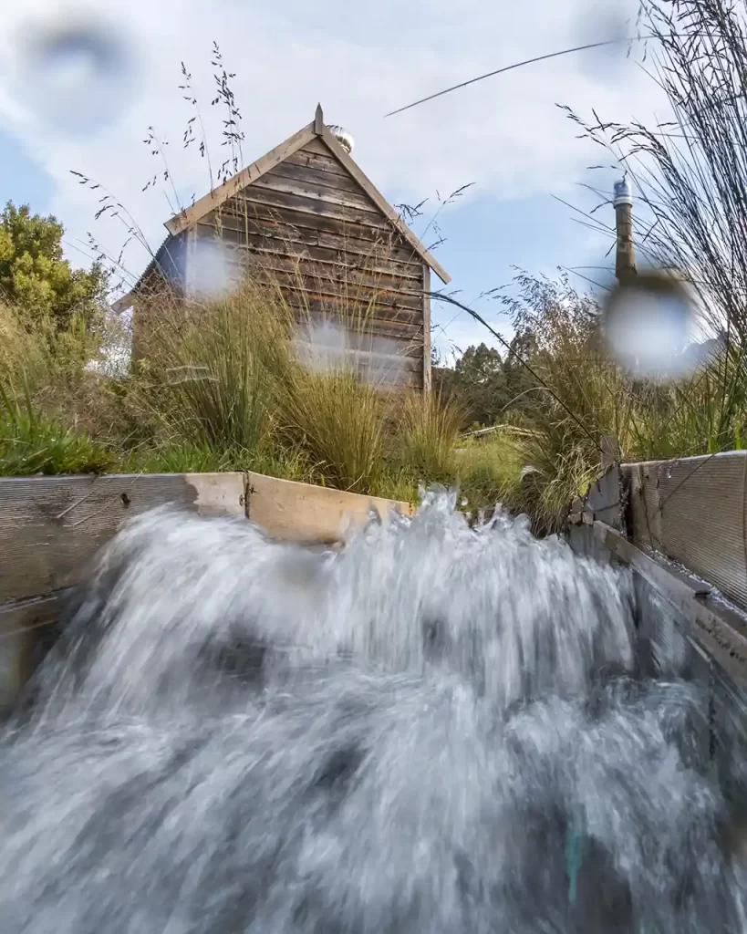 Water is rushing down the tail race from our timber micro-hydro generator shed.