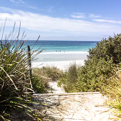 Steps are elading down to the Binalong Bay beach. in the distance, there are several people in the water.