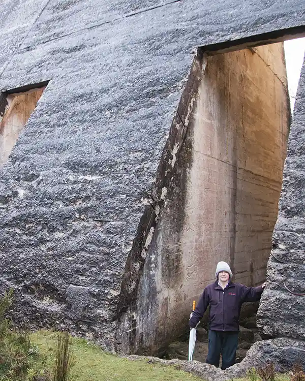 A man is standing in a large hole cut in the concrete wall of the Mt Paris dam, North East Tasmania