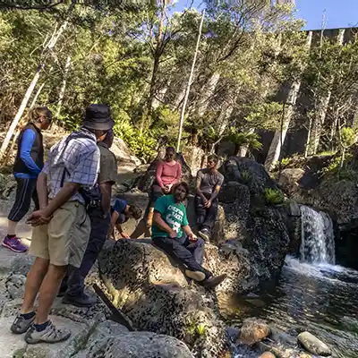 A group pof people, some standing and some sitting on rocks below the Mt Paris dam wall.