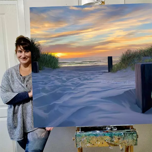 Jules Sharman is standing next to her painting of Henley Beach (SA). This is a painting of the beach at sunset.