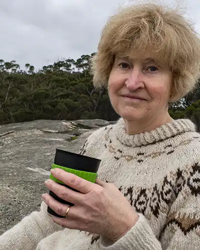 Christine is facing the camera with a cup of tea in her hand.