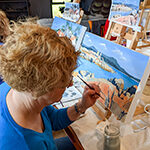 A woman working on an acrylic painting of a seacape.