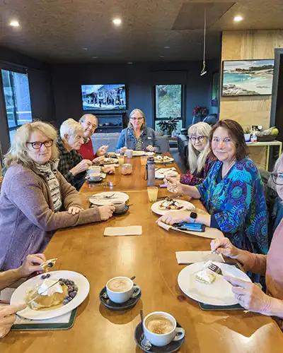 Eight art retreat students sitting around the breakfast table enjoying blueberry and cream pancakes.