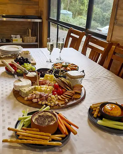 On a table is a selection of dips, biscuits, meats, cheeses and fruits and sparkling wine.
