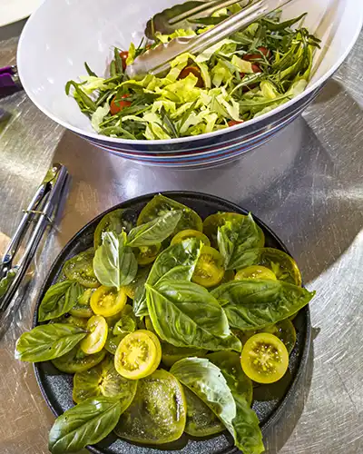 Sliced lime-green tomatoes are on a bed of sweet basil leaves.