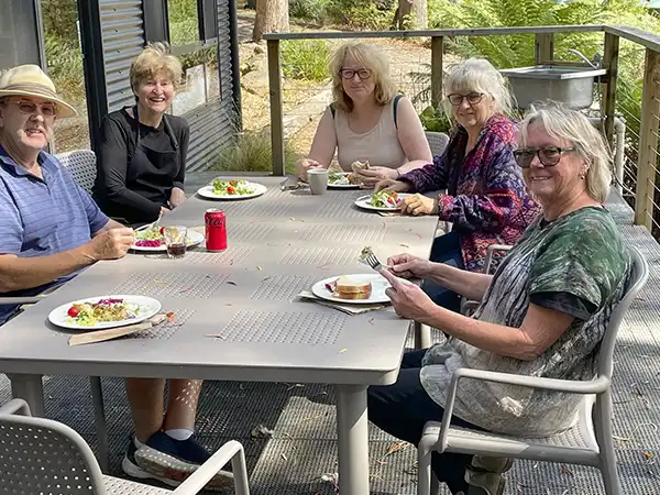 Art group participants sitting around an outdoor table eating lunch