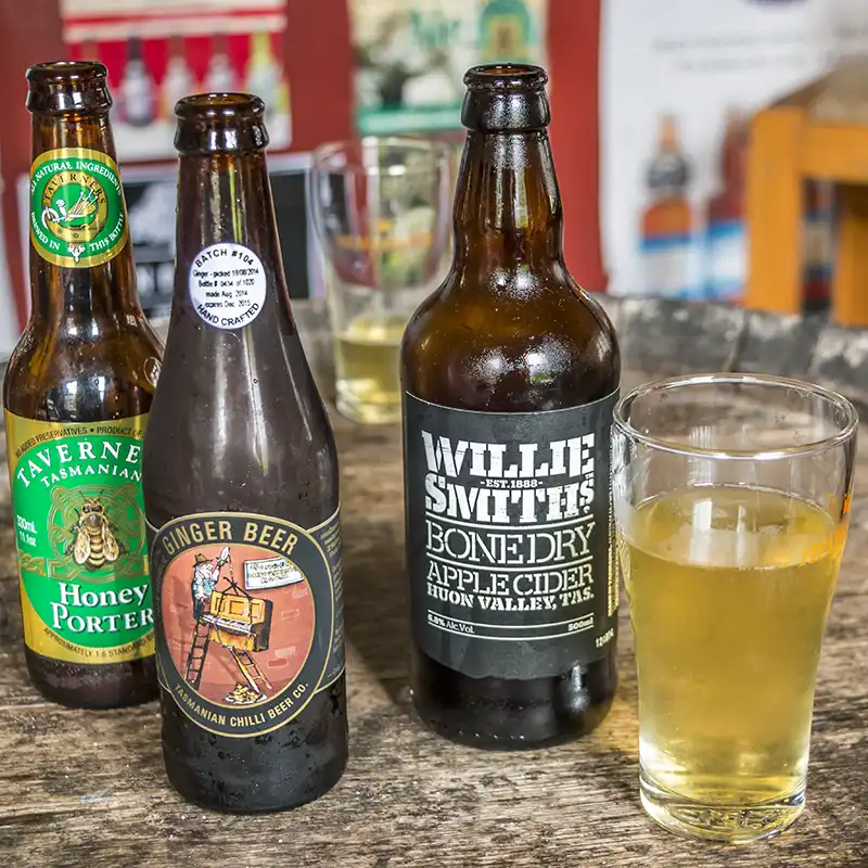 Three different bottles of craft brew and a full glass of cold cider
