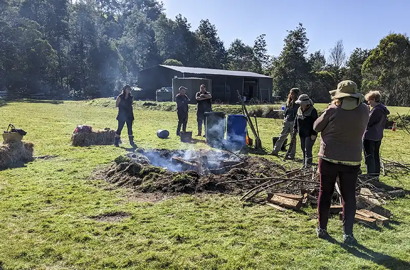 A group of seven people are standing around a fire pit where they are making biochar.