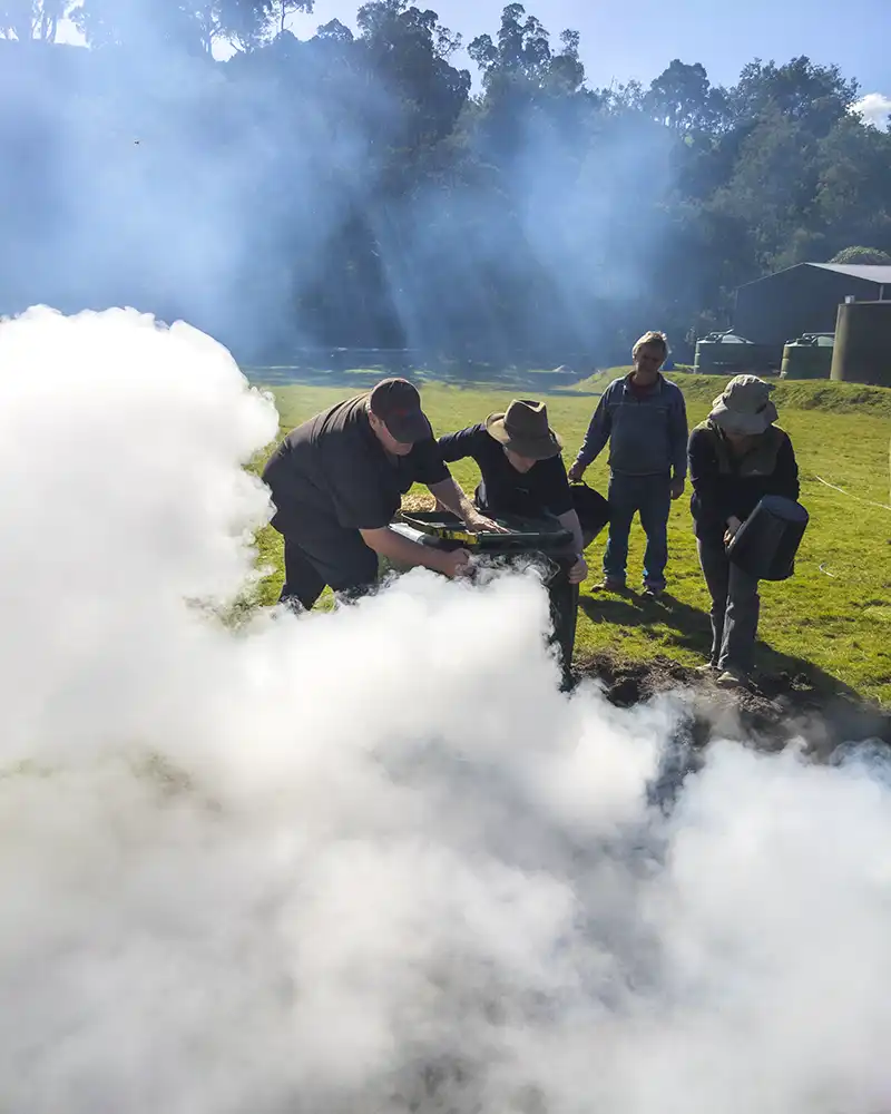 Four people are pouring bucket of water on to a small fire to make biochar.