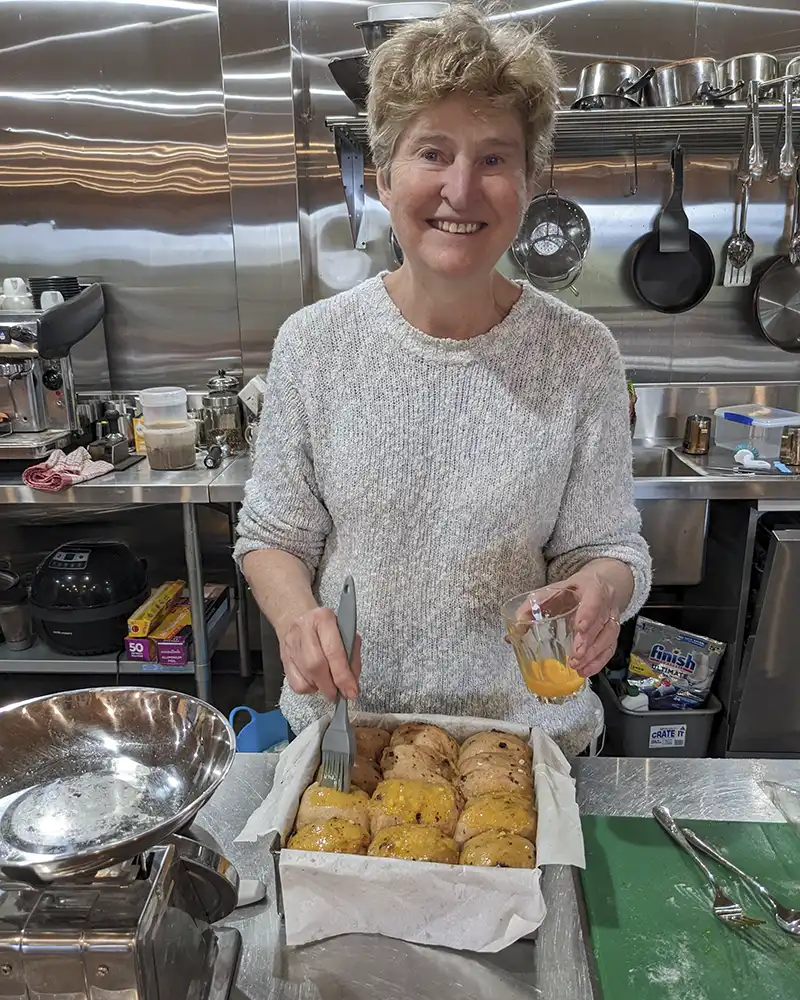 Christine is brushing the raw buns with an egg wash.