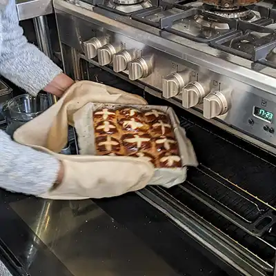 A baking tray filled with hot cross buns is being removed from a kitchen oven.