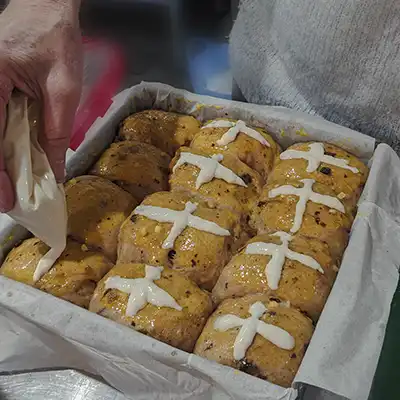 A plastic bag is being used to pipe the crosses onto the raw buns